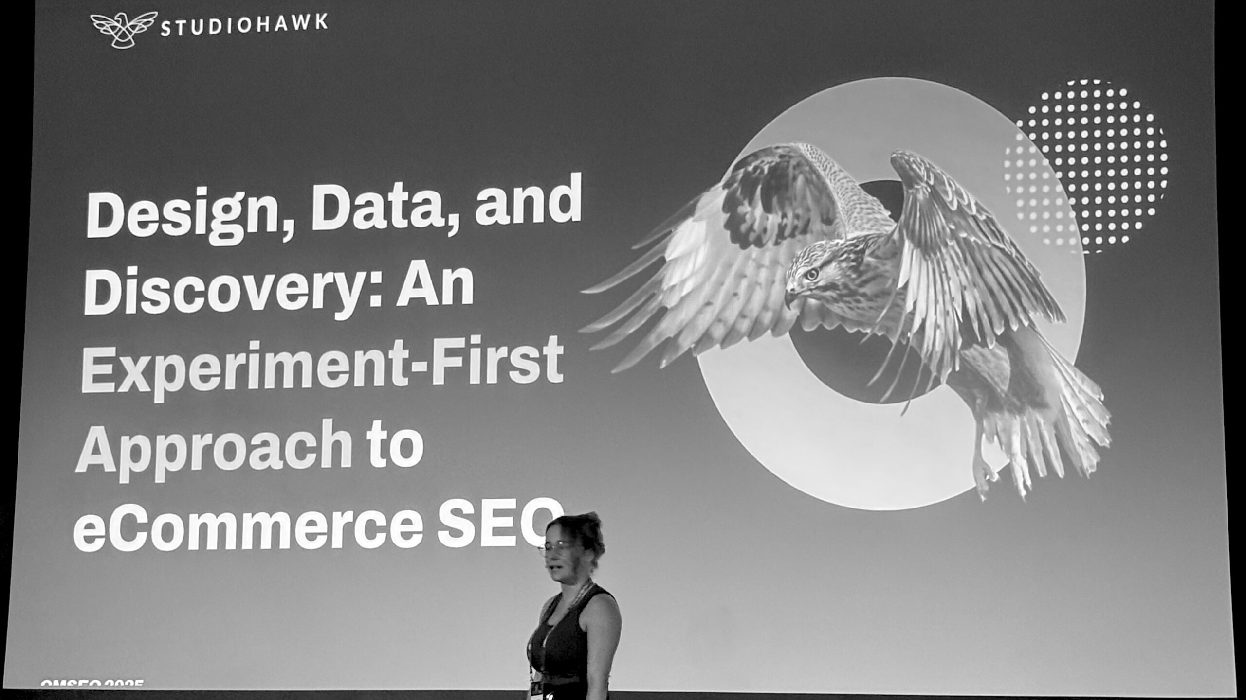 A presenter stands in front of a large SEO conference slide titled 'Design, Data, and Discovery' featuring a hawk graphic and bold typography.