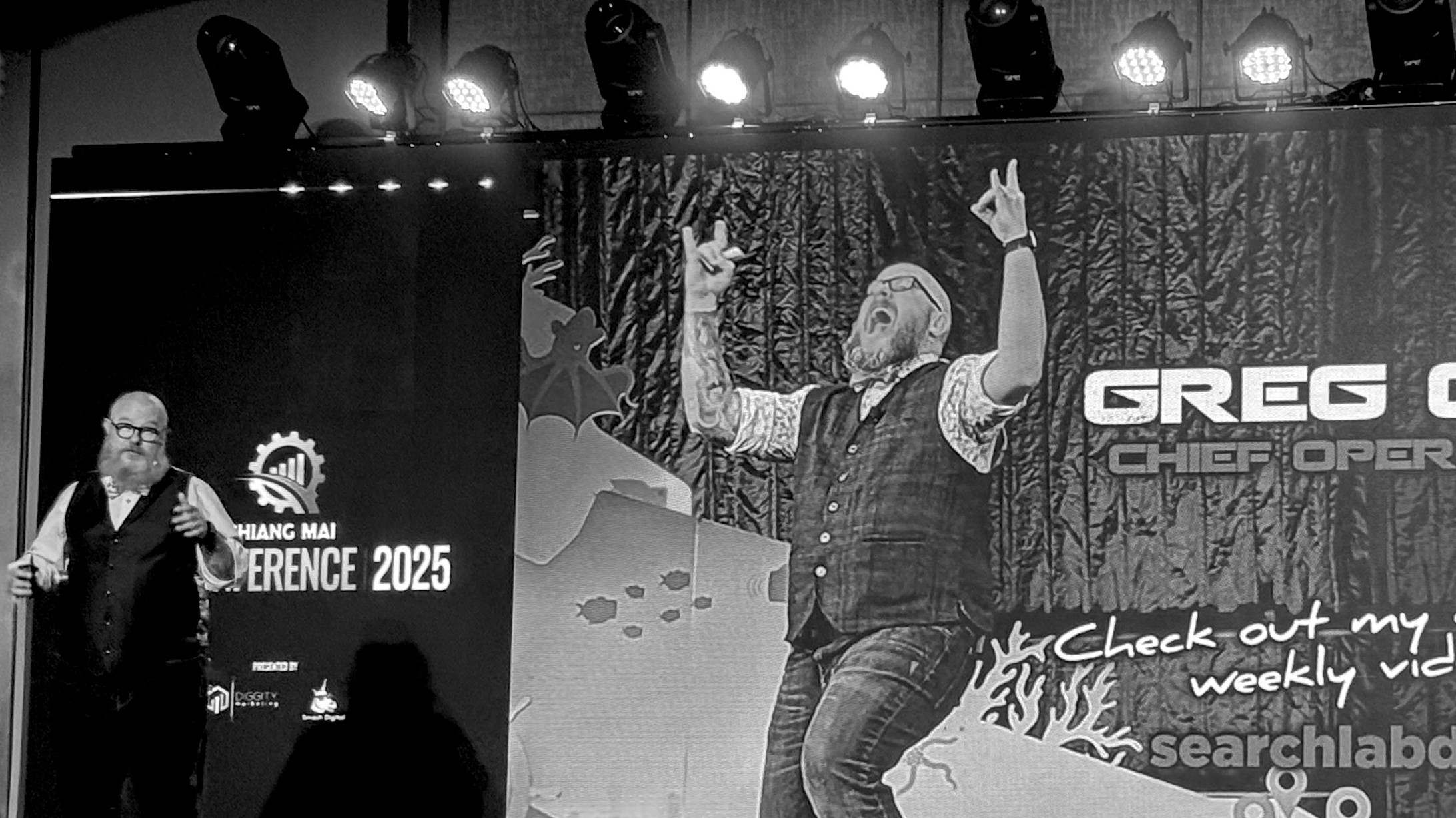 A charismatic speaker presents at the Chiang Mai SEO Conference 2025, standing beside a vibrant screen showcasing digital marketing visuals and event branding.